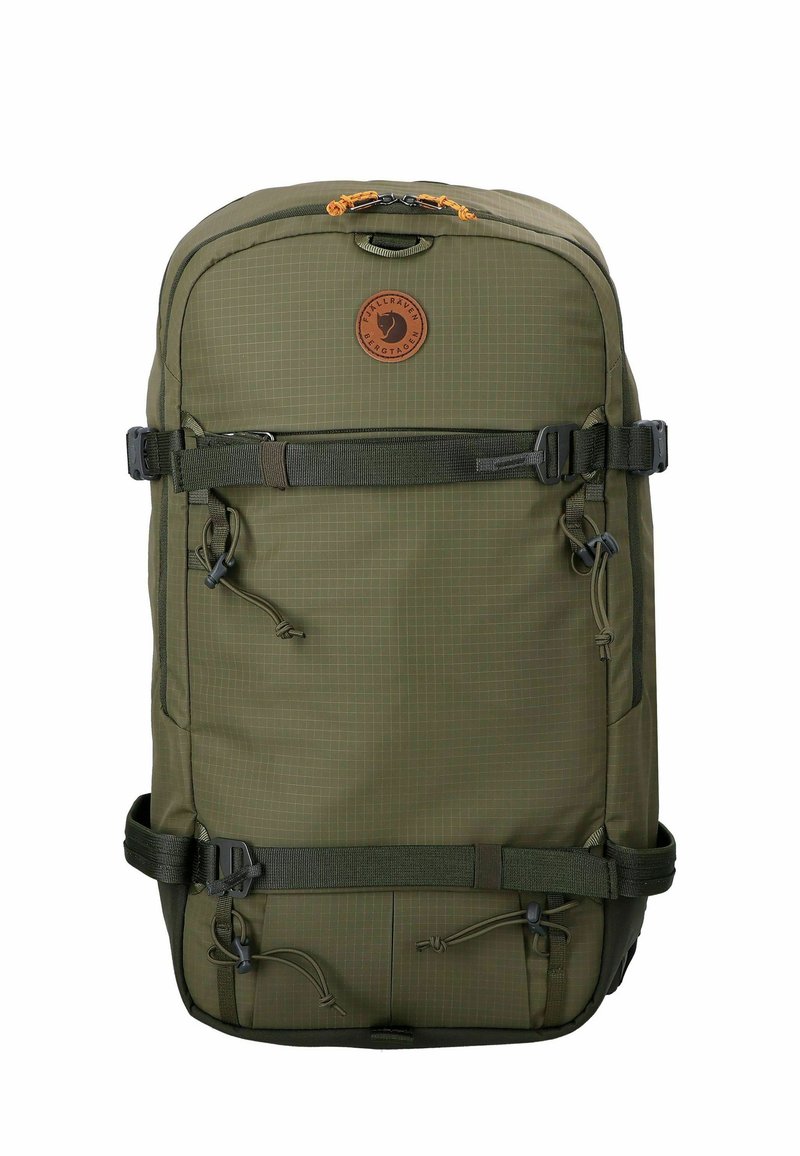 Mochila de color verde oliva hecha de material duradero. Presenta un patrón de rejilla, cierres de cremallera y hebilla, correas ajustables y un parche con el logotipo.