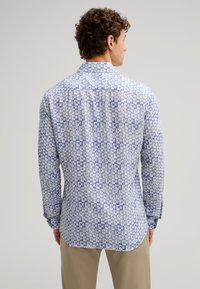 Camicia a maniche lunghe di colore azzurro chiaro con un motivo geometrico. Presenta un colletto, polsini con bottoni e un orlo curvo. Tessuto morbido.
