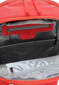 L'interno dello zaino in nylon rosso presenta un ampio scomparto, una fodera argentata, più tasche e una sezione con cerniera per ulteriore spazio di archiviazione.