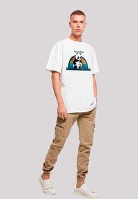 White oversized t-shirt featuring a panda graphic with the word "Nostalgia," paired with beige cargo pants and white sneakers.