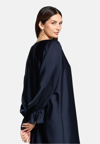 Robe en satin bleu marine avec une coupe ample, encolure ronde et manches longues avec des poignets froncés. Texture lisse avec un minimum de détails.