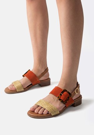 Pies con sandalias de punta abierta con correas delanteras tejidas en beige, correas medias de ante naranja con hebillas de carey, y tacones bajos gruesos marrones.