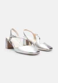 Silver metallic slingback heels with a square toe, chunky heel, and adjustable ankle strap. Smooth texture with minimal stitching detail.