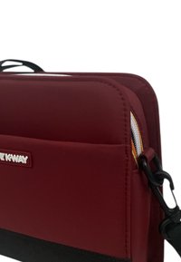 Borsa in poliestere rosso con superficie testurizzata, fondo nero a contrasto e cerniera bianca; presenta un logo e una tracolla rimovibile.