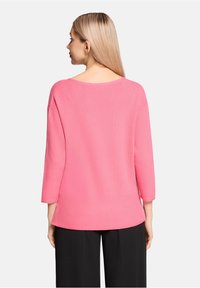 Pull en maille rose côtelée avec un col large et des manches trois-quarts, tissu texturé et ourlet inférieur légèrement évasé.