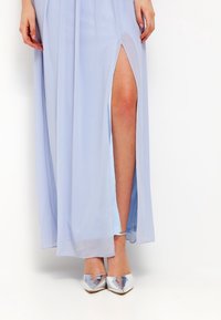 Maxi dress azzurro chiaro con spacchi laterali, tessuto fluido e texture liscia. Completato con tacchi a punta argentati.