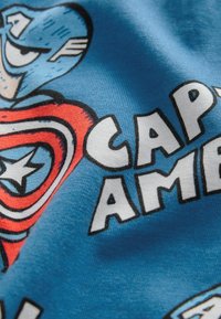 Nærbillede af blåt stof med trykt Captain America skjoldemblem og delvis tekst med "CAP AME."