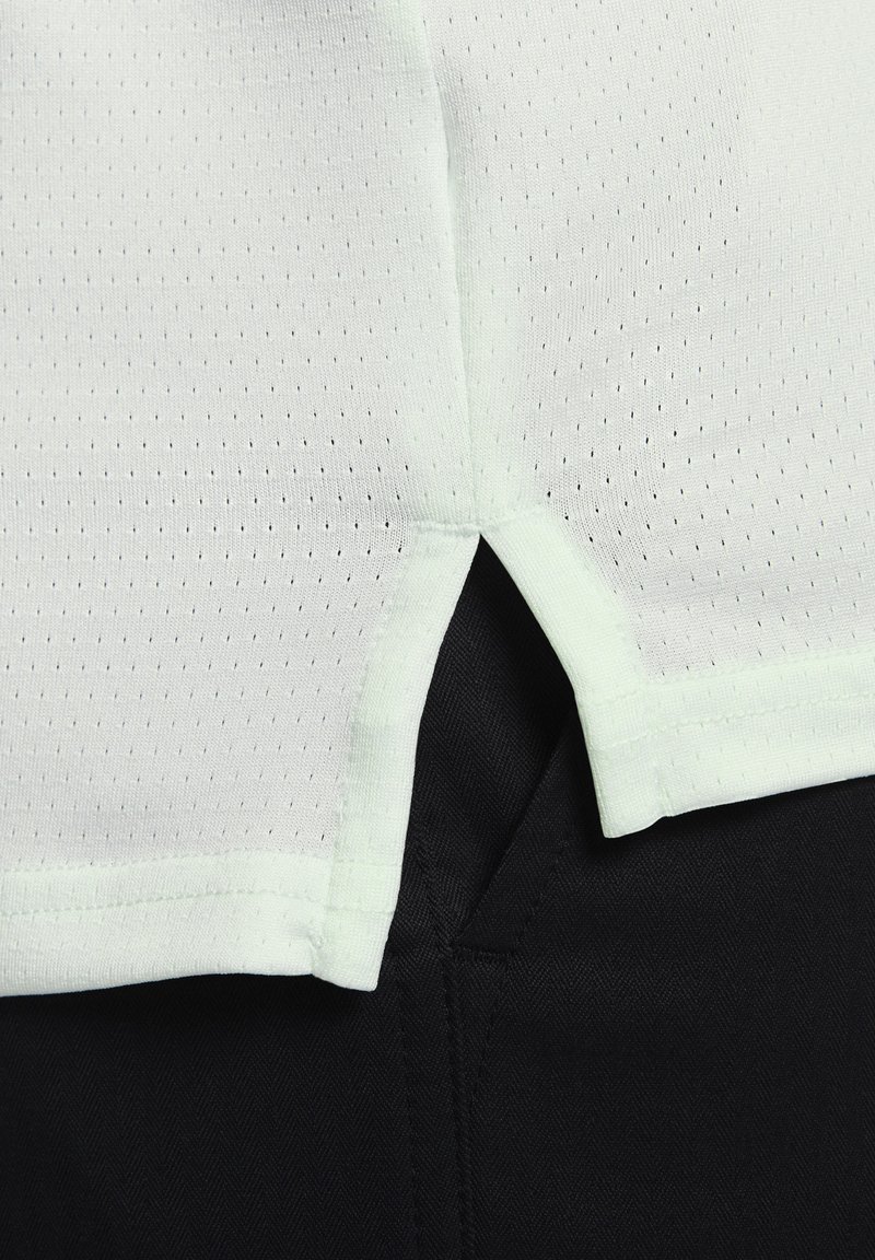 Hematoma perforada en color verde claro con aberturas laterales sobre una tela texturada negra, creando un contraste de color y material.