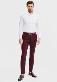 Biała koszula z długim rękawem zestawiona z bordowymi spodniami na miarę i ciemnymi loafersami. Strój ma wyraźnie zarysowany fason i gładką teksturę.