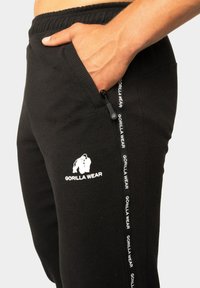 Zwarte joggers gemaakt van gestructureerde stof, met een zijrits zak en wit "Gorilla Wear" logo op het linkerbeen.