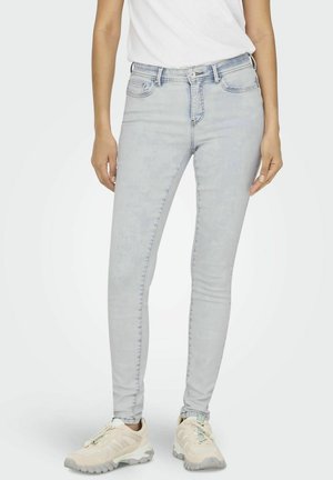 Světlé skinny džíny vyrobené z denimu, s vysokým pasem a jemným vyblednutím, spárované s béžovými sportovními botami.