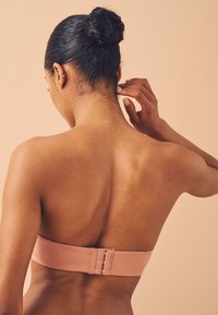 Strapless bh van lichtbruin materiaal met een gladde afwerking, voorzien van een haak-en-oogsluiting op de rug en een minimalistisch ontwerp.