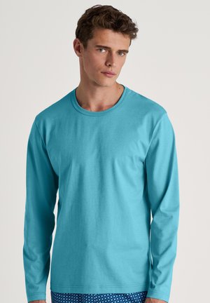 Türkises langärmliges T-Shirt mit rundem Halsausschnitt und glatter Baumwolltextur. Kombiniert mit gemusterten blauen Shorts mit kleinen weißen Formen.