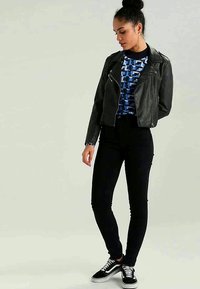 Black leather motorcycle jacket over a blue geometric-patterned top, paired with dark skinny jeans and black sneakers.