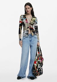 Dugi rukavi, košulja s višestrukim uzorcima i dubokim V-izrezom, u kombinaciji s širokim svjetloplavim farmerkama i šarenom torbom s uzorkom.