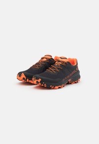 Black and orange trail running shoes with textured fabric, rugged outsole, and contrasting laces, featuring a camo pattern on the sole.