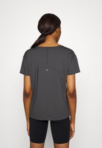 Mörkgrå, kortärmad tränings-T-shirt med rundad halsringning, subtil detalj på ryggen och platta sömmar, tillsammans med svarta, åtsittande shorts.