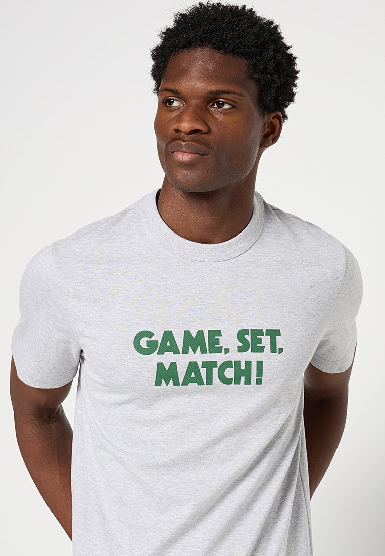 Graues Baumwoll-T-Shirt mit auffälligem grünen Text, der "SPIEL, SATZ, MATCH!" lautet. Rundhalsausschnitt und kurze Ärmel.