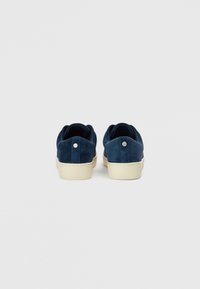 Σκούρα μπλε σουέντ αθλητικά παπούτσια με χαμηλή κορυφή, λαστιχένιες σόλες σε κρεμ χρώμα και μικρό ασημένιο διακοσμητικό στη φτέρνα πίσω. Ομαλή υφή.