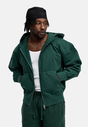 Green zip-up hoodie with a spacious hood and front pockets. Made from soft fabric, features ribbed cuffs, and a relaxed fit.