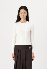 Knit white sweater with a cable pattern, round neckline, and ribbed hem, paired with a dark pleated skirt featuring double buckle accents.