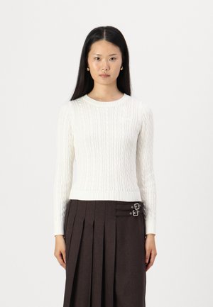Pull en tricot blanc avec un motif torsadé, col rond et ourlet côtelé, associé à une jupe plissée foncée avec des accents de double boucle.
