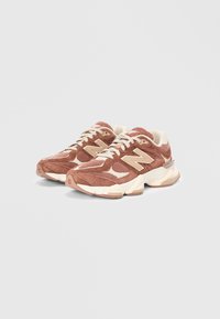 Baskets marron clair avec une tige texturée, des accents crème et une semelle épaisse. Présente un logo 'N' bien en évidence et un design à lacets.