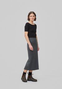 Haut noir ajusté, jupe midi grise à la texture lisse, présentée avec des bottines marron à talons mi-bas avec des panneaux latéraux élastiques et des bouts ronds.