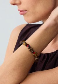 Tijgeroog armband met rode accentbedels, voorzien van gladde, natuurlijke vormen in aardetinten op een blote pols.