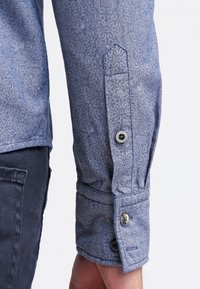 Long-sleeve button-up shirt featuring a light blue fabric with a subtle pattern, cuff with a button closure, and contrasting stitching.