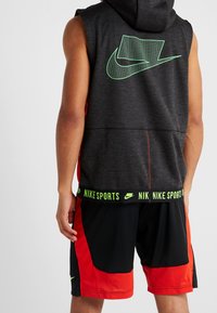 Czarny bezrękawnik z kapturem z zielonym logo Nike na plecach oraz czerwono-czarne spodenki z zielonym pasem "NIKE SPORTS".