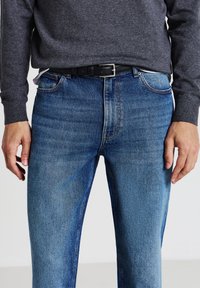 Jeans in denim blu con un finish leggermente sbiadito, caratterizzati da un taglio dritto, design a cinque tasche e una cintura nera con una fibbia metallica quadrata.