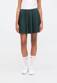 Zaļa plisejota svārku ar elastīgu jostu, apvienota ar rozā Nike logo zeķēm un baltām kedām. Vienkāršs, sportisks dizains.