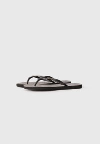 Des tongs noires avec des lanières élégantes et une semelle grise texturée, présentant un subtil accent doré près des lanières. Design léger.