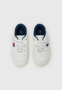 Baskets blanches avec accents bleus et rouges, en cuir, semelle en caoutchouc et sangle Velcro. Présentent des trous de ventilation et un détail de marque.