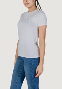 T-shirt bianca a maniche corte con un design grafico testurizzato. Realizzata in morbido cotone, con scollatura rotonda e vestibilità rilassata. Abbinata a jeans blu.