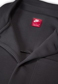 Szary T-shirt Nike z kołnierzykiem, metką wskazującą rozmiar M oraz fakturowaną tkaniną z minimalnymi detalami szwów.