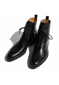 Botas de tobillo de cuero negro con un acabado suave, puntera redondeada y cordones en la parte frontal. Presentan un interior marrón claro y detalles de costura mínimos.