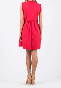 Abito rosso senza maniche con dettagli arricciati sulle spalle, corpetto aderente, vita arricciata e gonna svasata. Abbinato a sandali con tacco alto color crema.