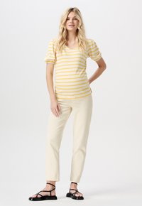 Gul och vitrandig kortärmad topp med V-halsringning, ihopparad med ljusbeiga raka byxor och svarta sandaletter med remmar.