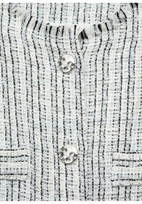 Tissu blanc texturé avec des rayures verticales noires et des boutons argentés martelés irréguliers sur le devant d'un vêtement.