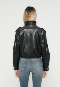 Sort læder cropped jakke med skulderpuder og en indsnævret kant. Glat tekstur, enkelt design, parret med blå denim jeans.