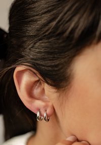 Srebrne kolczyki w kształcie koła prezentowane na tle teksturowanego ucha. Kolczyki są okrągłe, gładkie i wypolerowane, delikatnie odbijające światło.