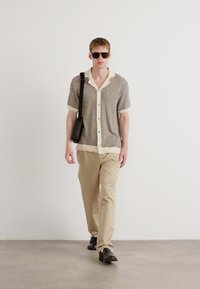 Short-sleeve knit shirt with a multicolor pattern and cream collar, paired with beige trousers and black shoes, accessorized with sunglasses.