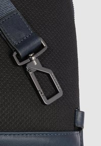 Correa de nailon azul marino con un cierre metálico plateado, con un material negro texturizado. Acento de cuero liso en la parte inferior.