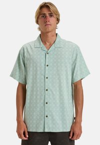 Camicia a maniche corte con bottoni di colore verde menta chiaro e motivo floreale bianco, dotata di colletto a camicia e cinque bottoni marroni sul davanti.