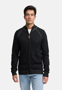 Sort lynlåssweater med et tekstureret strikkemønster, der har en høj krave, ribbede manchetter og en lynlåsholder af træ.