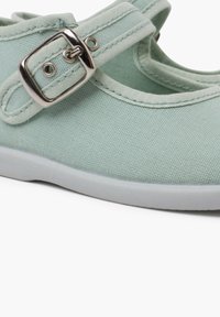 Zapato de lona verde menta con punta redonda, correa ajustable con hebilla y suela de goma blanca. Tela texturizada y detalles de costura en contraste.