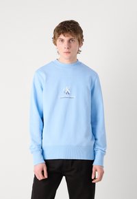 Felpa azzurra realizzata in misto cotone, con colletto a girocollo con coste, maniche lunghe e stampa bianca del logo sul petto. Abbinata a pantaloni neri.