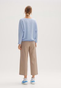 Jasnoniebieski sweter o fakturze z szerokim dekoltem, zestawiony z beżowymi spodniami o szerokich nogawkach oraz szarymi sneakersami z niebieskimi akcentami.